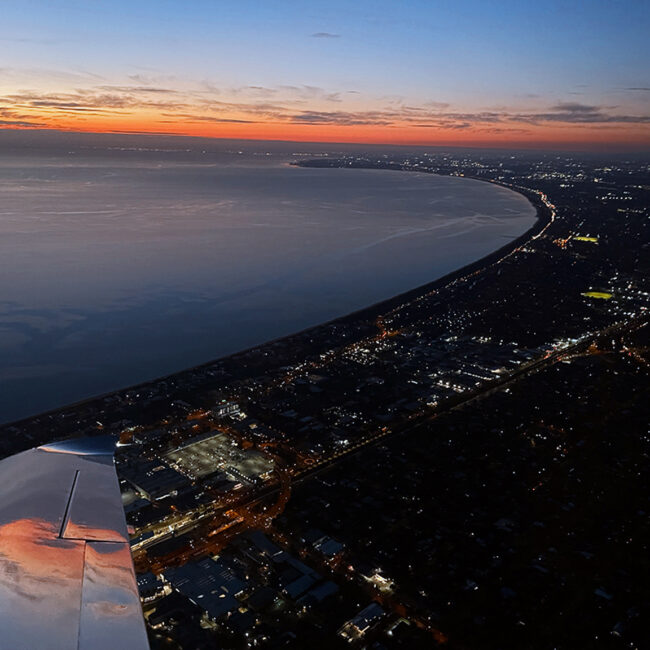 Aerial view of Melbourne coastline at dusk from a light aircraft, illustrating the visual conditions suitable for Night VFR flight.