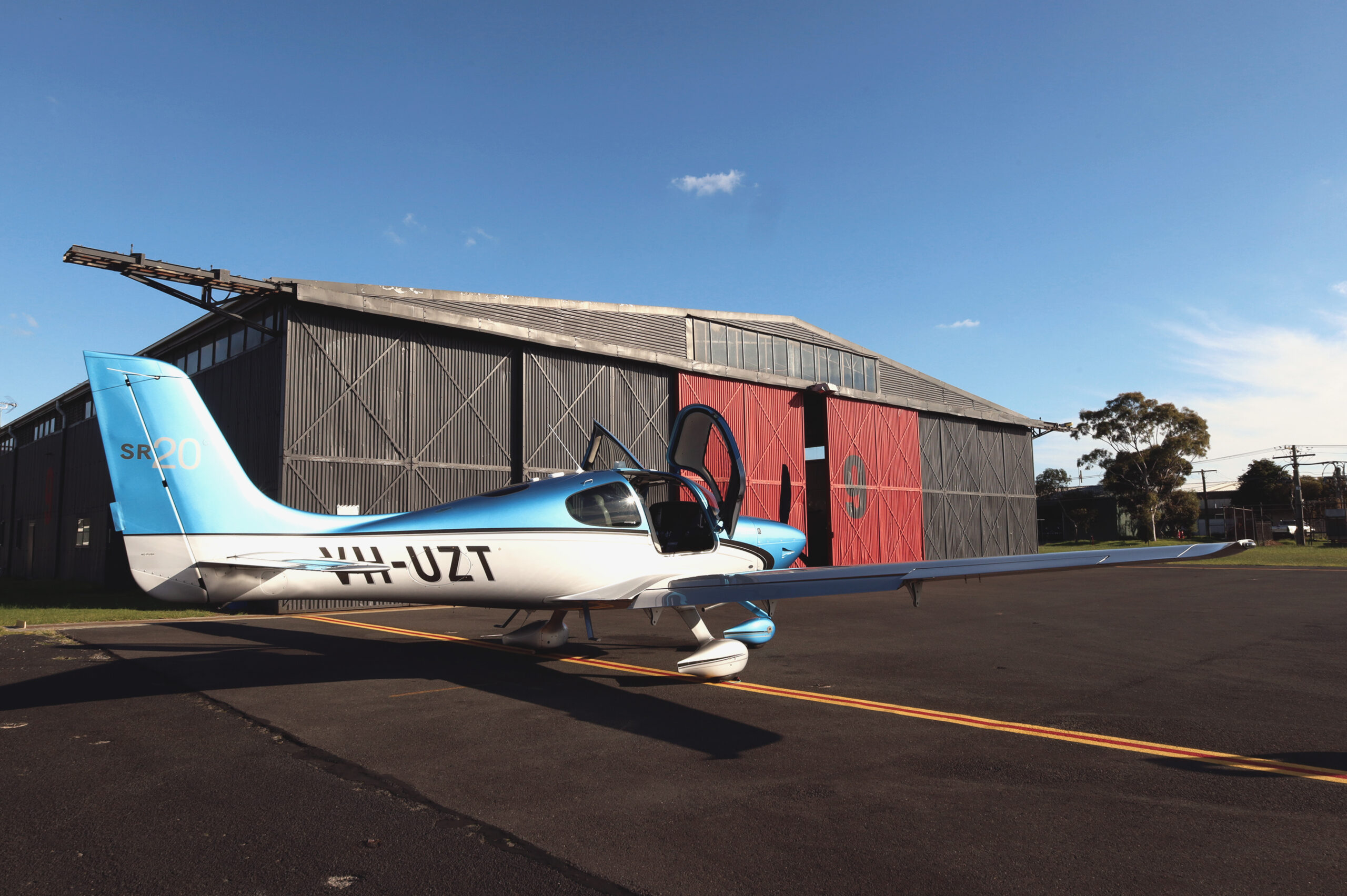 Cirrus SR20 aircraft parked outside Avia Aviation hangar under a blue sky with scattered clouds.