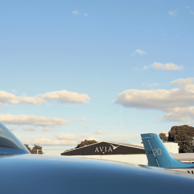 Cirrus SR20 aircraft parked at Avia Aviation hangar under a clear blue sky with scattered clouds.