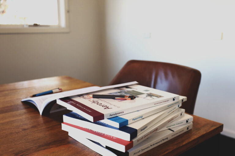 Stack of aviation theory books on a wooden desk, including titles on aerodynamics, navigation, and meteorology, used for pilot training study.
