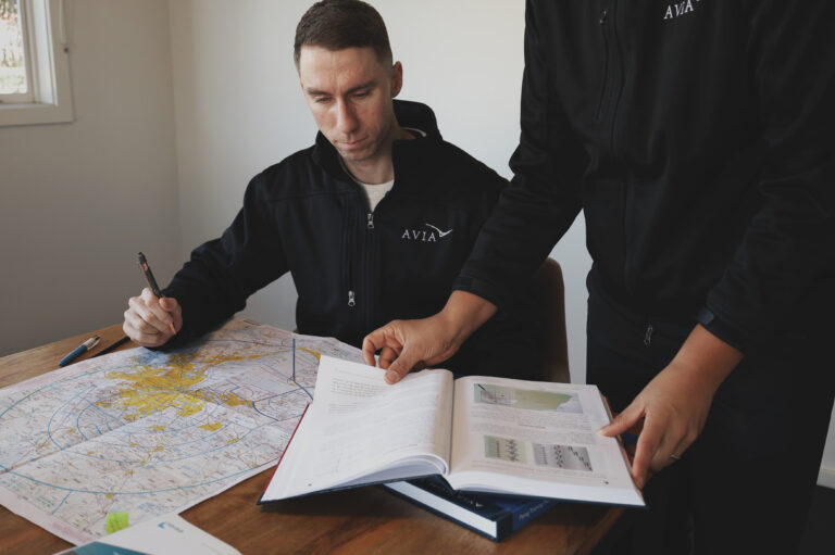 Student pilots in Avia Aviation uniforms reviewing flight planning charts and medical certification requirements during ground school preparation.