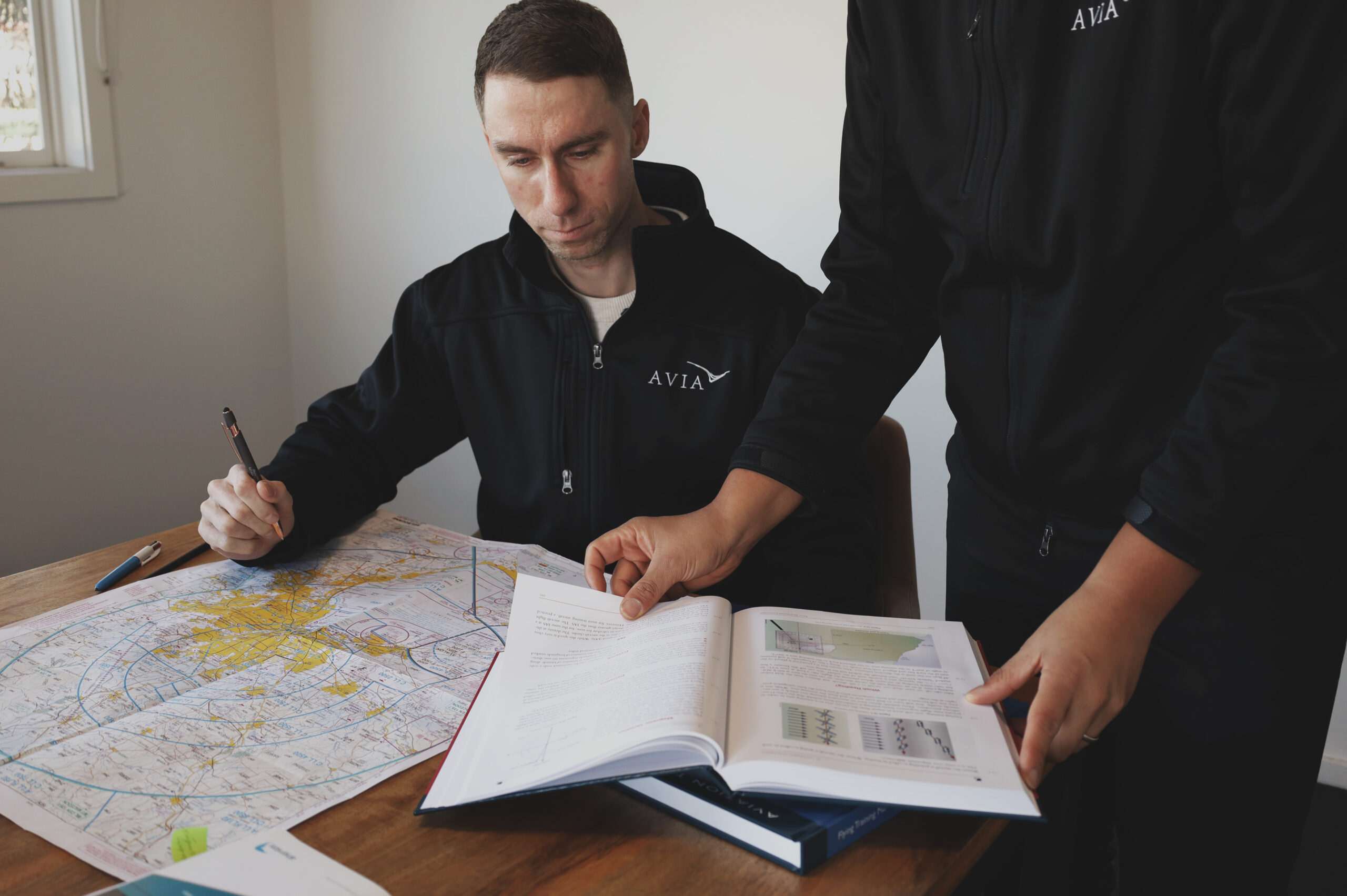 Student pilots in Avia Aviation uniforms reviewing flight planning charts and medical certification requirements during ground school preparation.