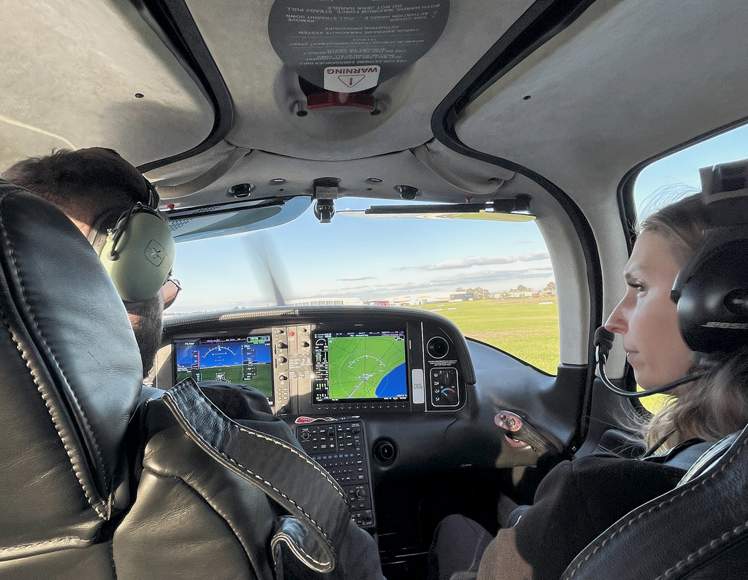 Flight instructor and student pilot seated in a Cirrus SR20 cockpit, reviewing instruments during a pre-takeoff briefing on a clear day.