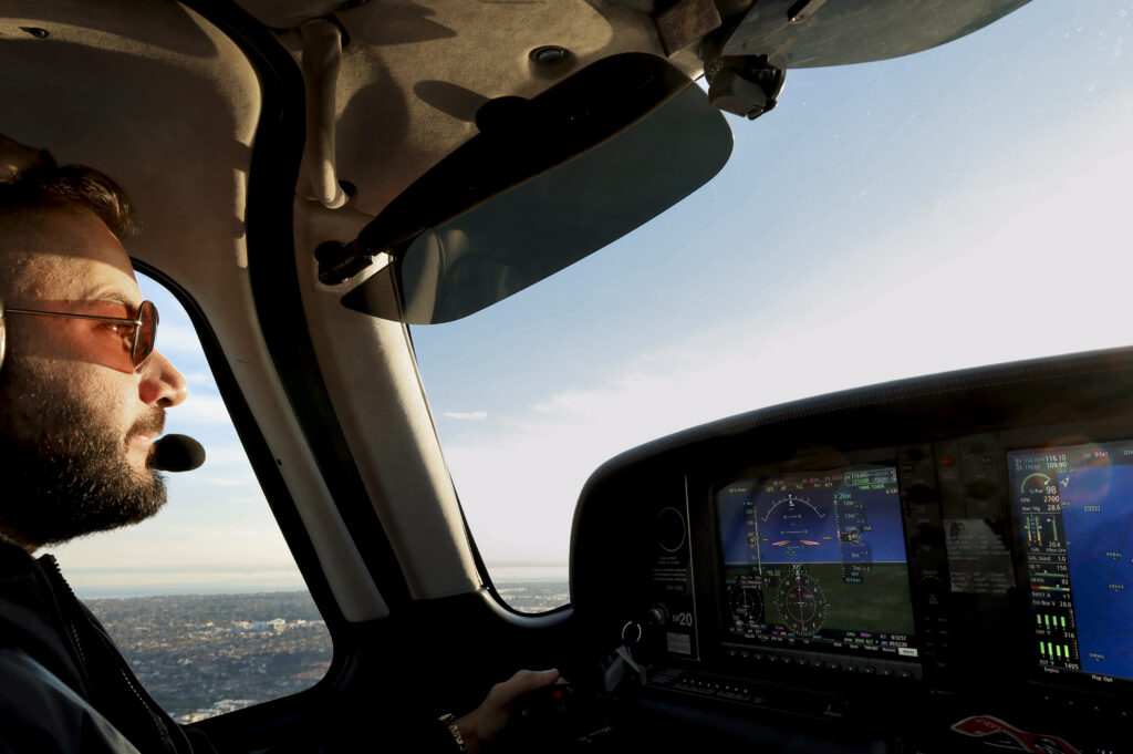 Pilot in headset flying a light aircraft in daylight, focused on cockpit instruments and horizon during mid-flight.