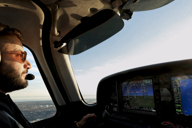 Pilot in headset flying a light aircraft in daylight, focused on cockpit instruments and horizon during mid-flight.